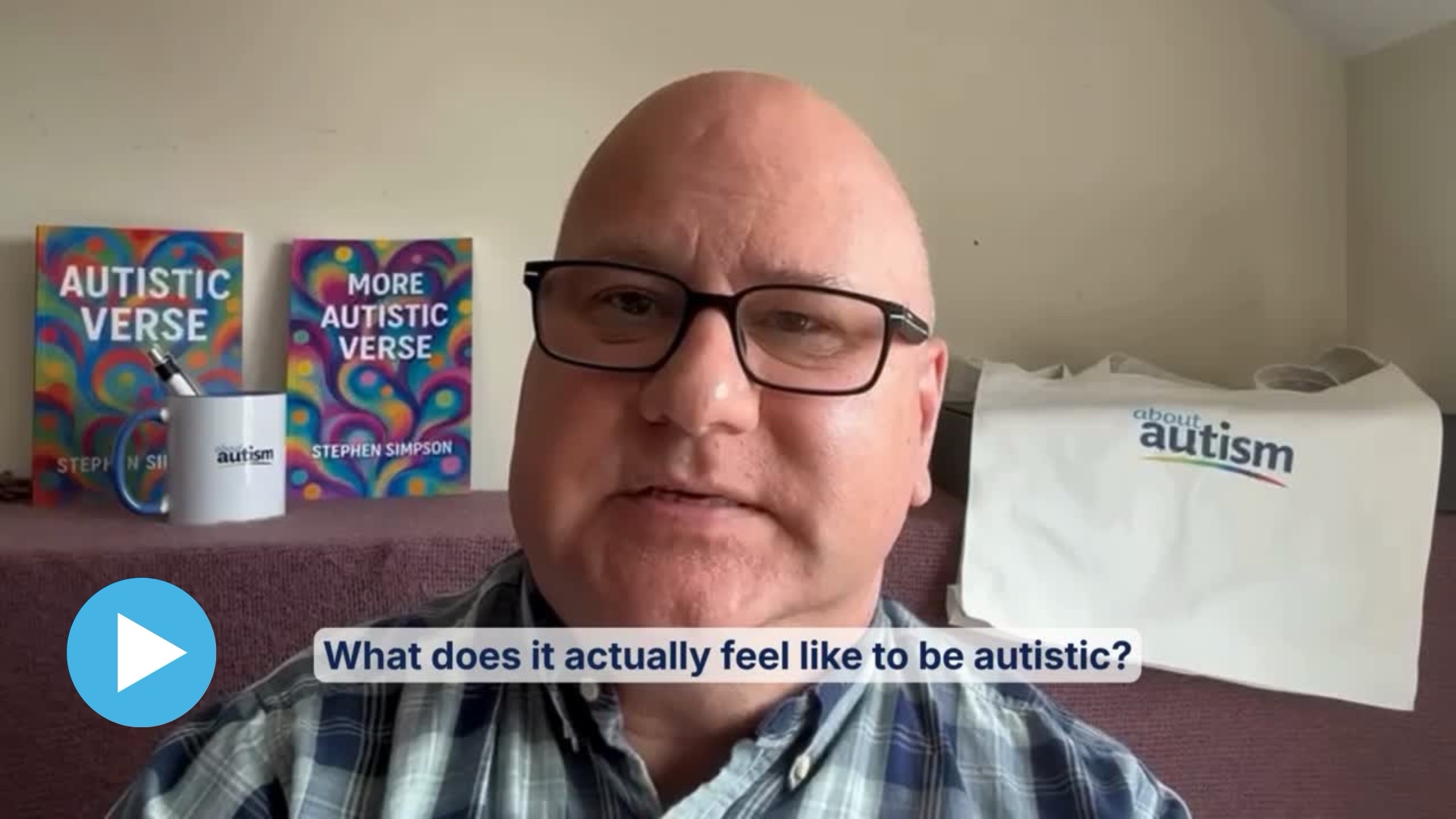 Stephen Simpson speaking to camera with his books Autistic Verse and More Autistic Verse and an About Autism mug and tote bag; on-screen caption reads ‘What does it actually feel like to be autistic?’